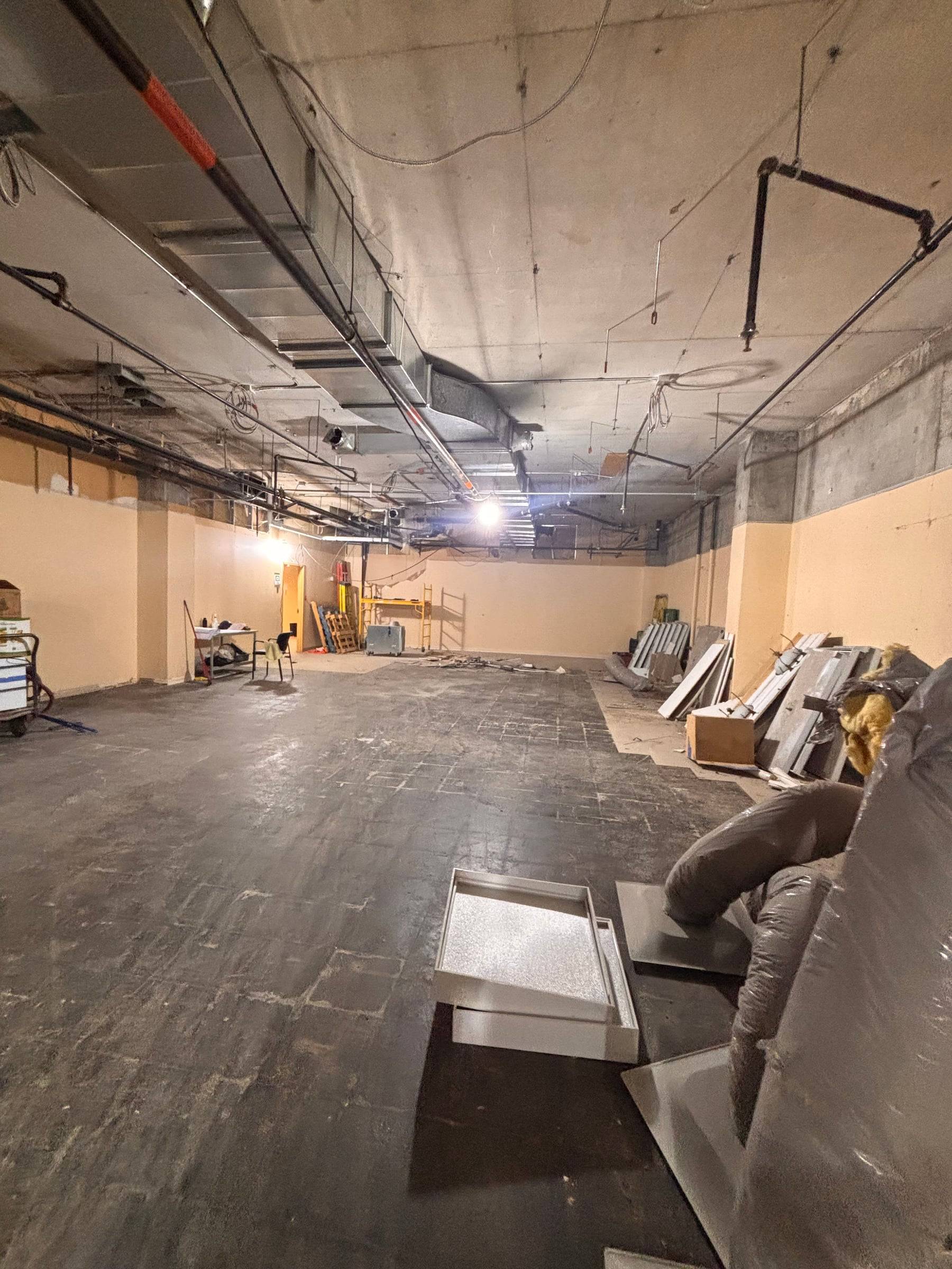 Grand local entièrement dégarni : dalle de béton, conduits et gicleurs apparents