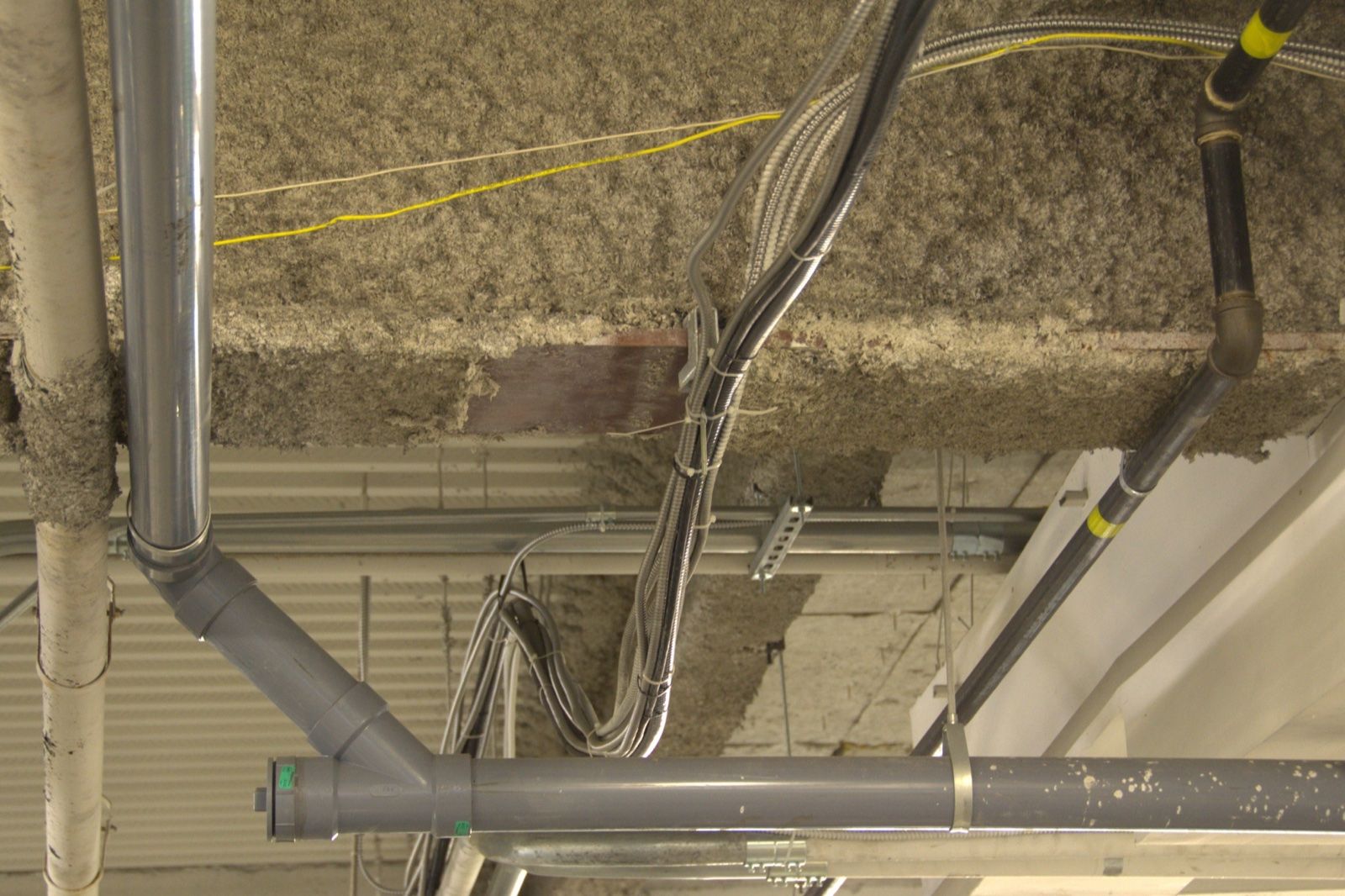 Fibrous spray-applied fireproofing on a ceiling structure, damaged in places