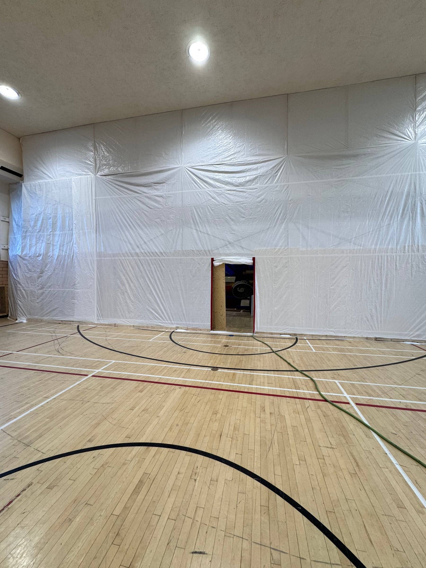 Gymnase dont un mur complet est confiné au polyéthylène, avec une porte d'accès à l'aire de travail