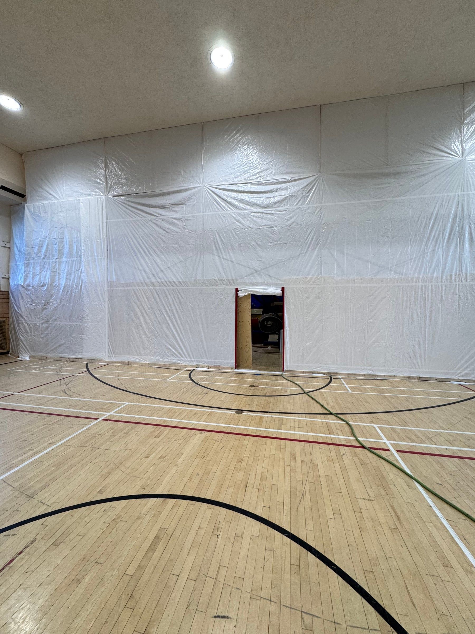 Gymnasium with one full wall sealed in polyethylene and an access door to the work area