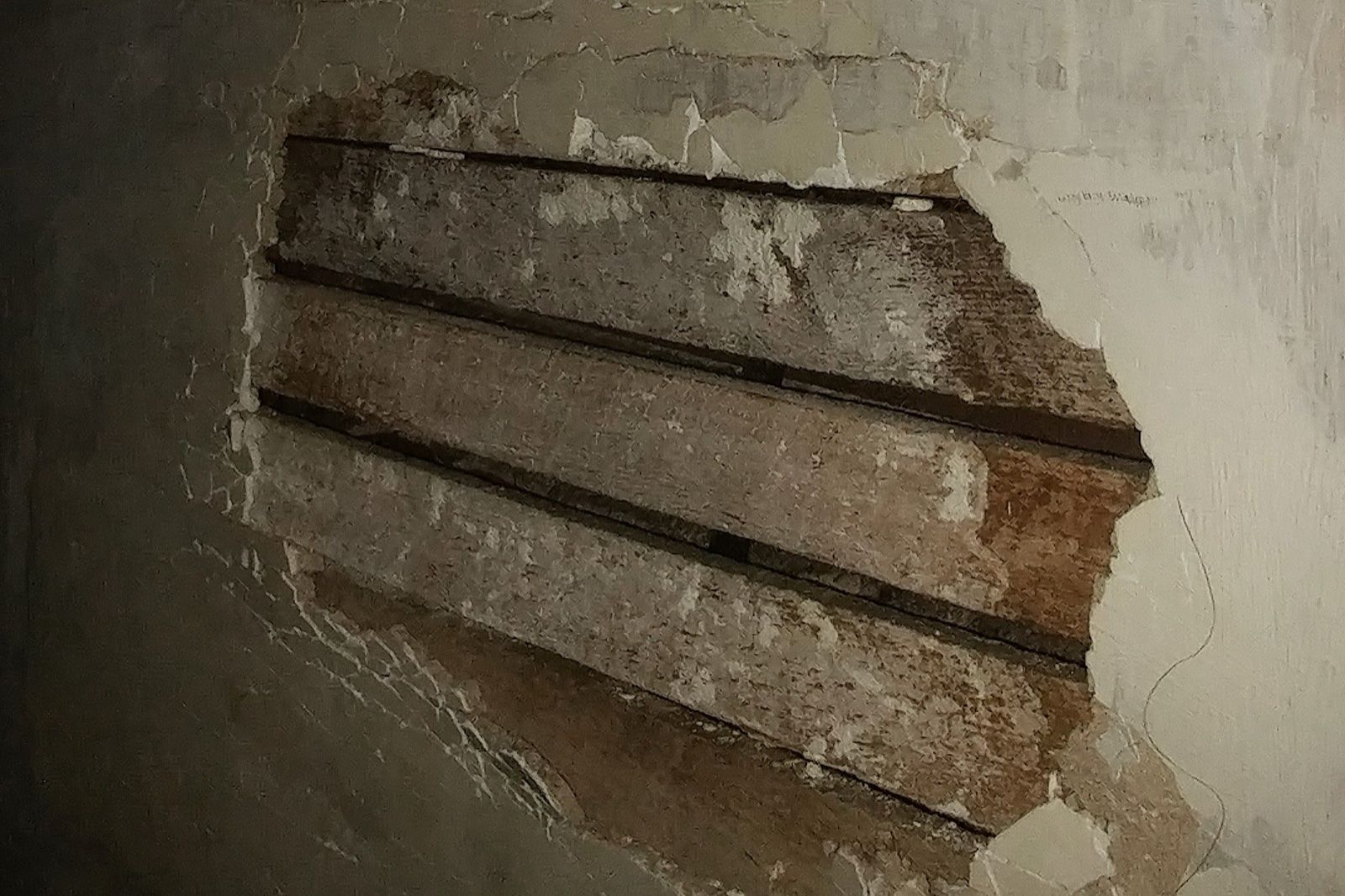 Old plaster wall with a hole showing the wood lath