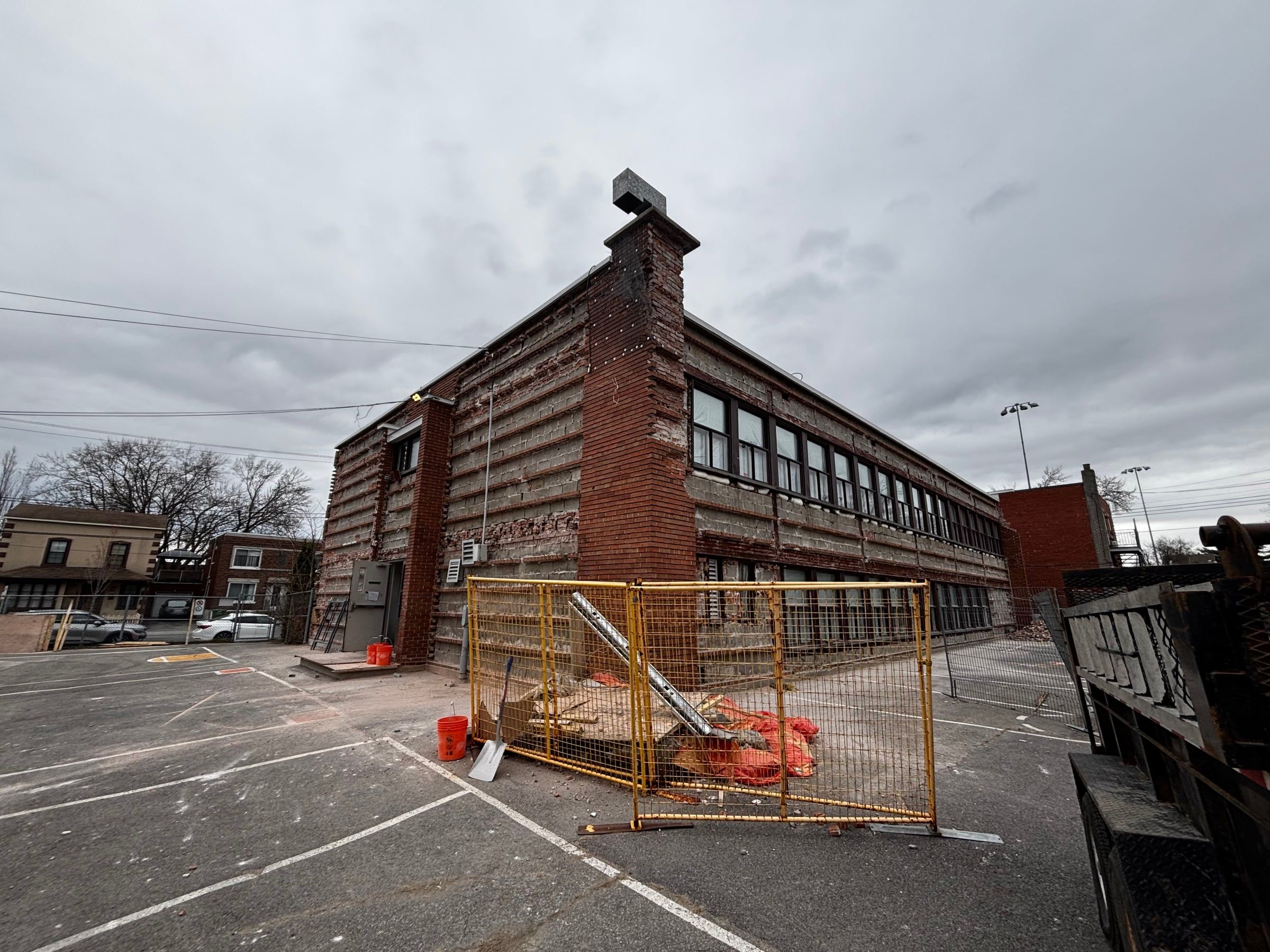 Two-storey school with its exterior brick cladding being removed, fenced work area at ground level