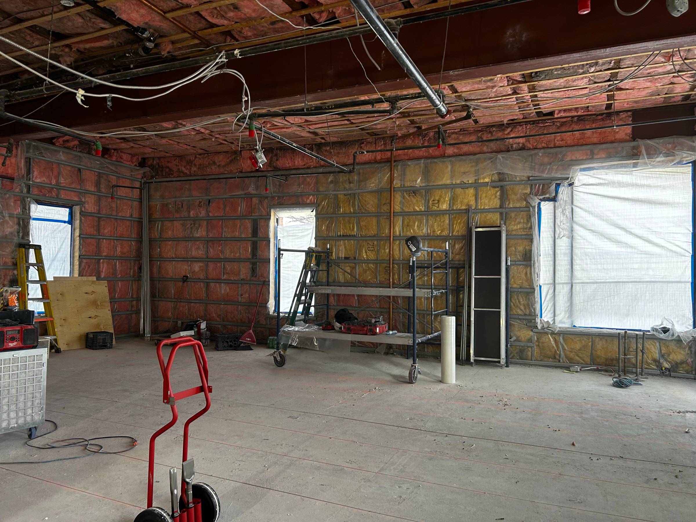 Local dégarni jusqu'aux murs de brique et à l'isolant, plafond ouvert jusqu'à la structure, échafaudage roulant sur place